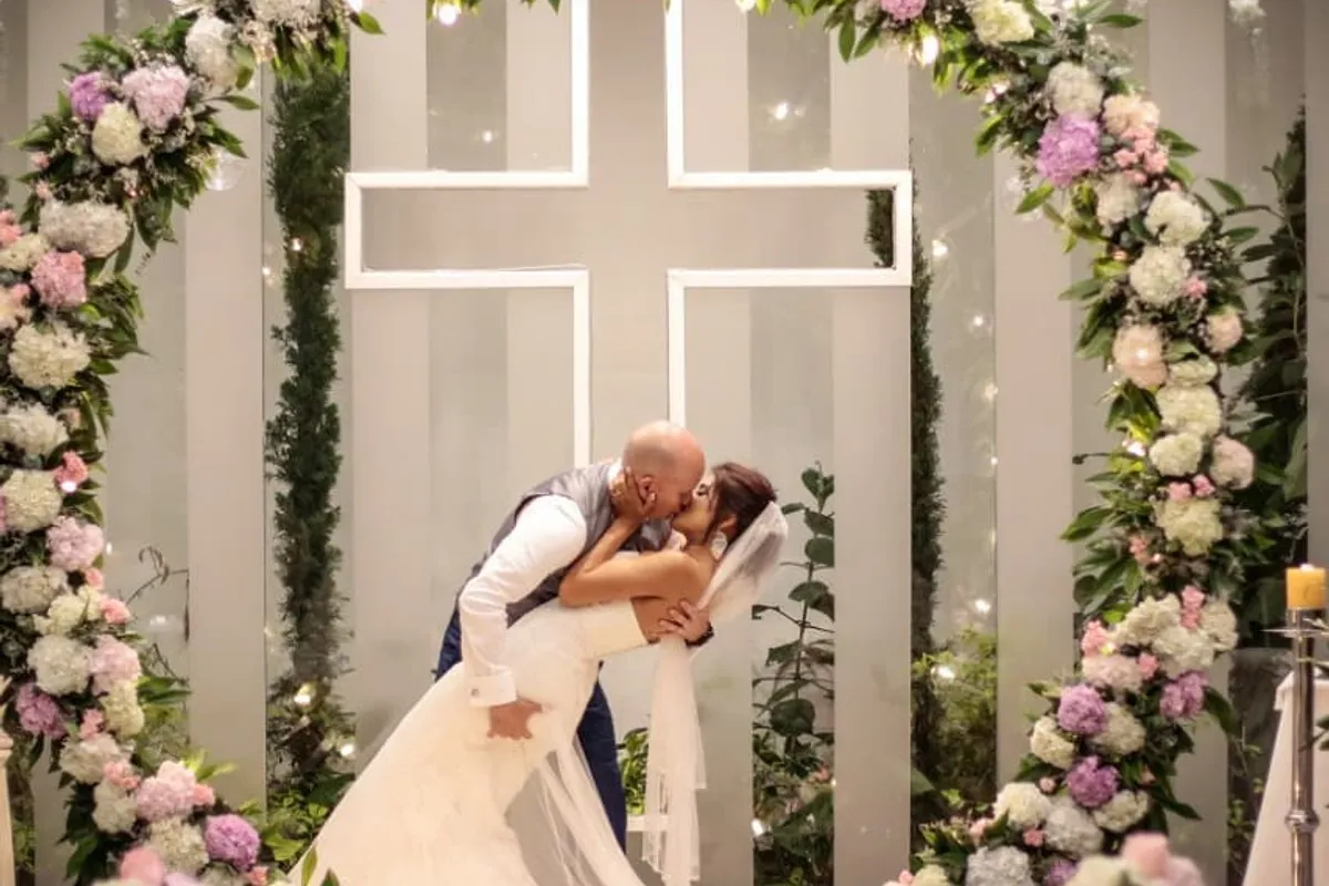 Pareja de novios besándose bajo un arco floral en su boda