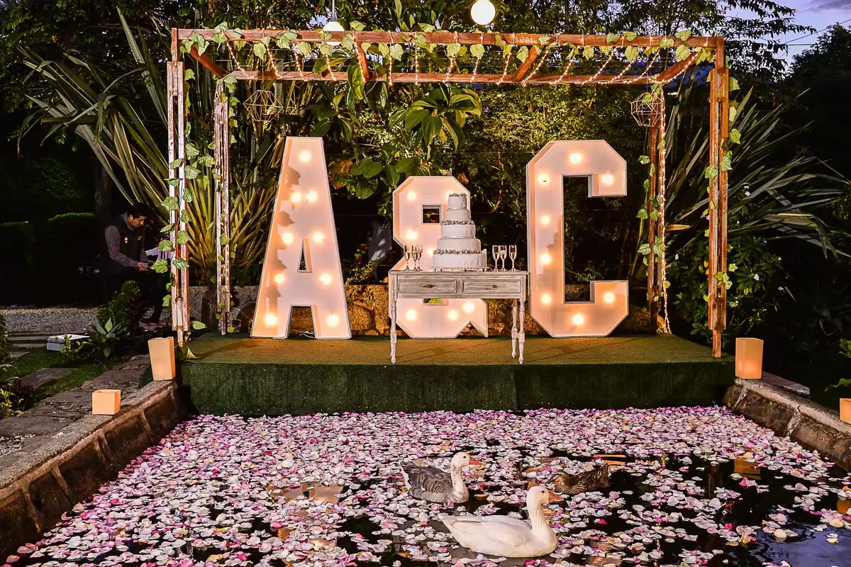 Pastel de boda blanco decorado junto a letras luminosas en un jardín